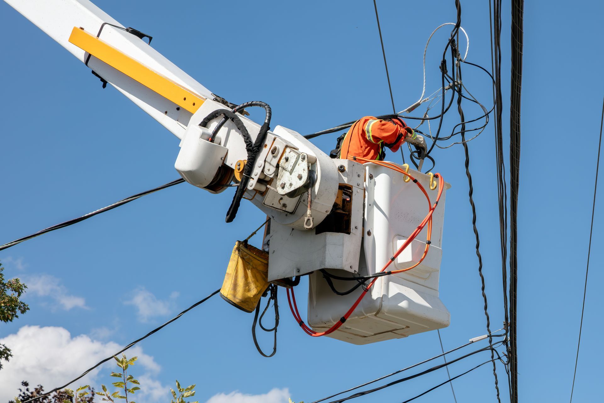 Utility worker in orange gear repairing power lines in a bucket truck against a blue sky