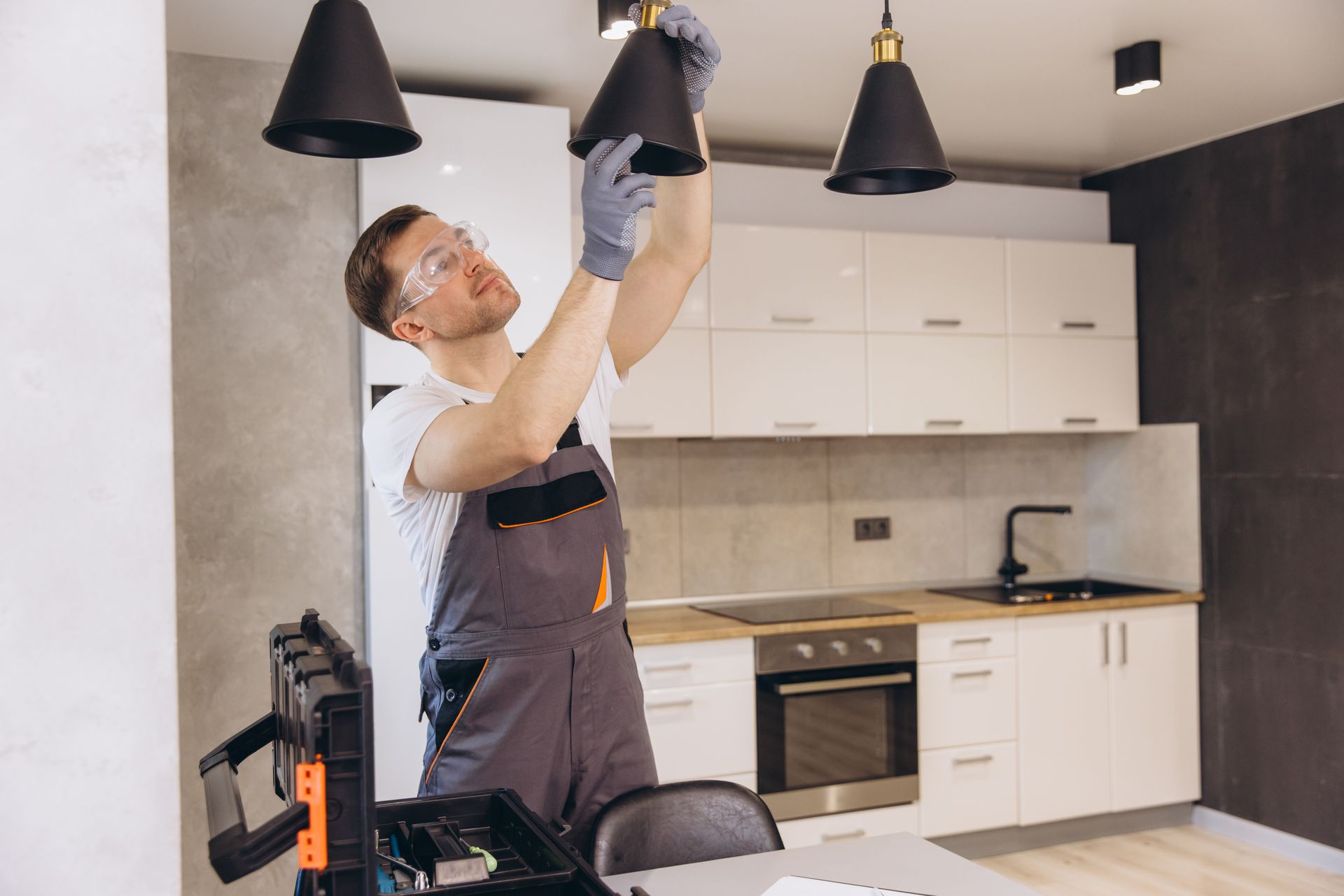 Technician adjusting a black pendant light in a modern kitchen with white cabinets