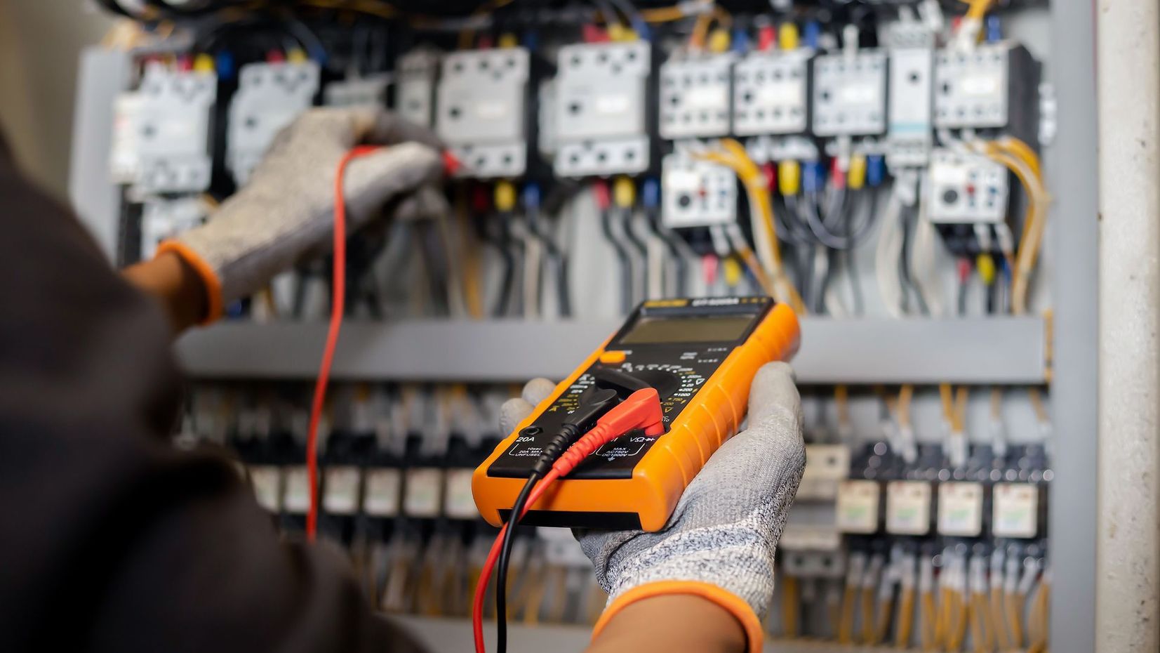 Technician testing an electrical control panel with a digital multimeter and red probe wires