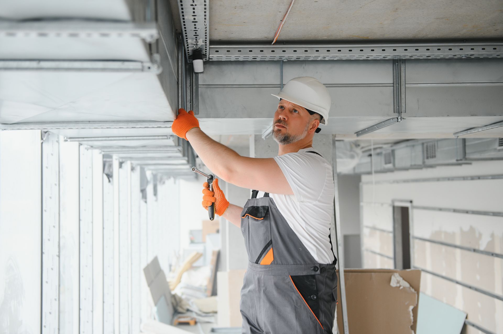 Worker in white hard hat using a tool to install ceiling fixtures in a construction site