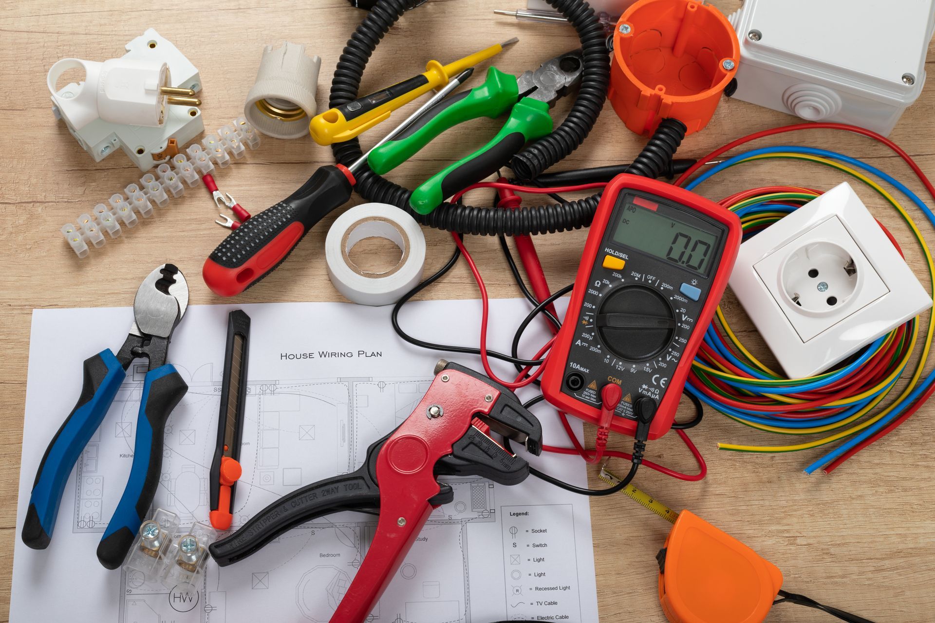 Assorted electrical tools, wires, outlets, and plugs spread across a workbench with diagrams.