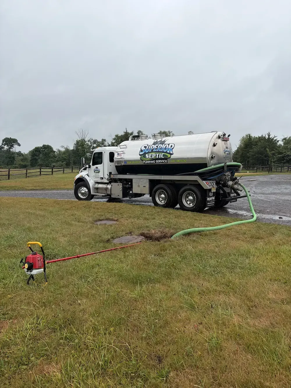 Septic truck pumping liquid into a grassy field with hoses laid out under an overcast sky