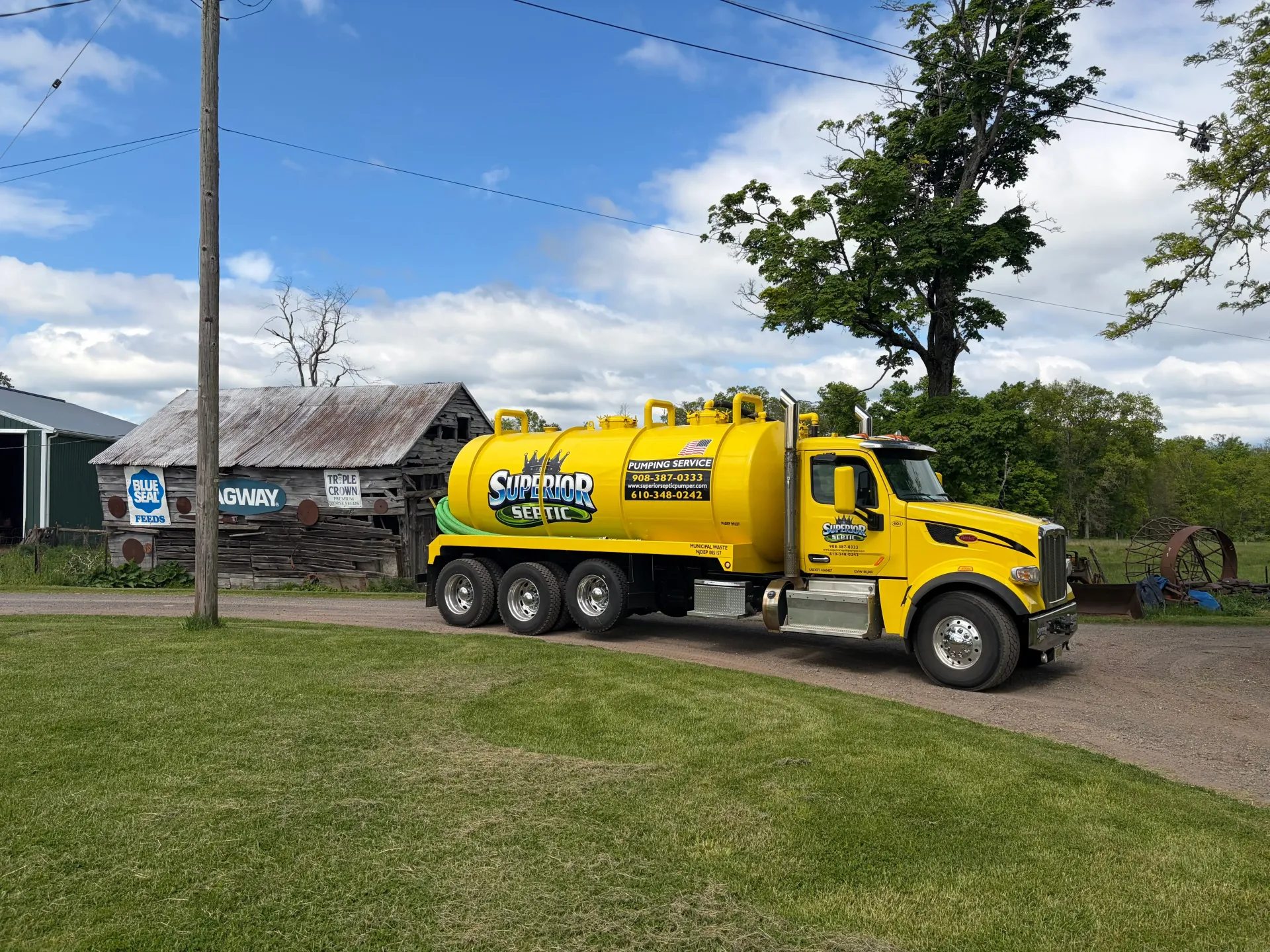 Yellow vacuum truck parked on a gravel driveway beside a house on a sunny day