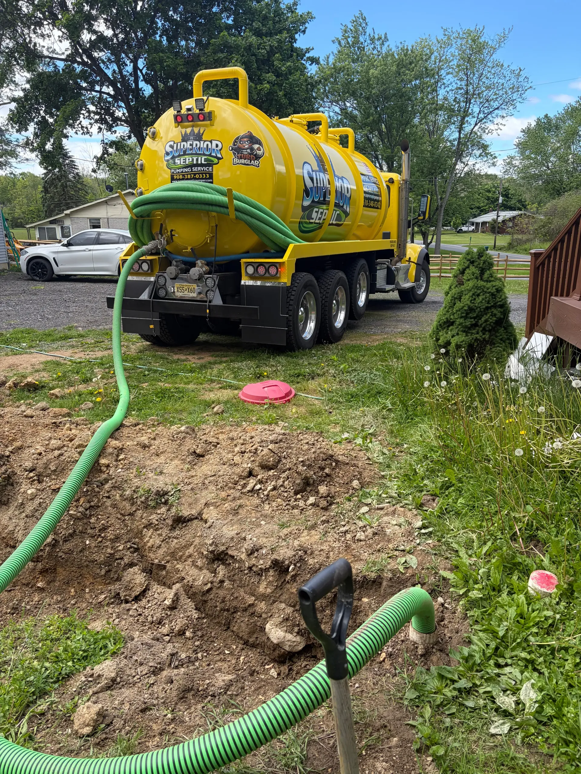 Yellow vacuum truck parked beside a lit building at dusk, with hoses laid across the ground.