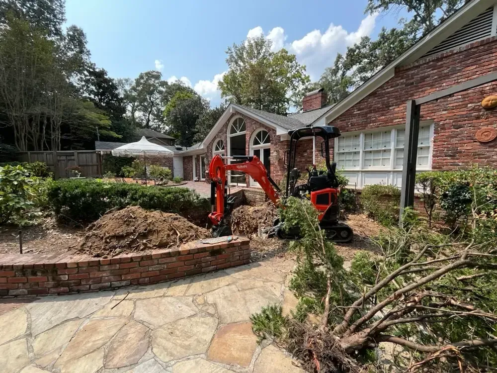 Orange excavator working in a landscaped yard beside a brick building and stone walkway