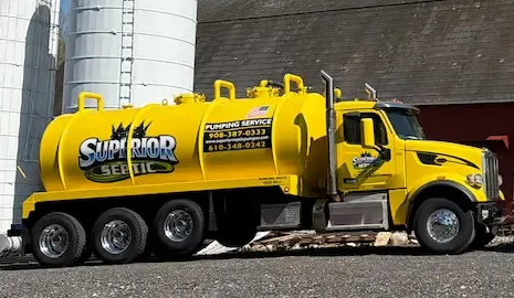 Yellow vacuum tanker truck parked by white silos, labeled “Sutherland Septic.”