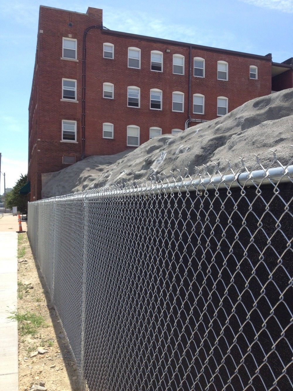 Brick building behind a chain link fence and a pile of gravel. Sunny day.