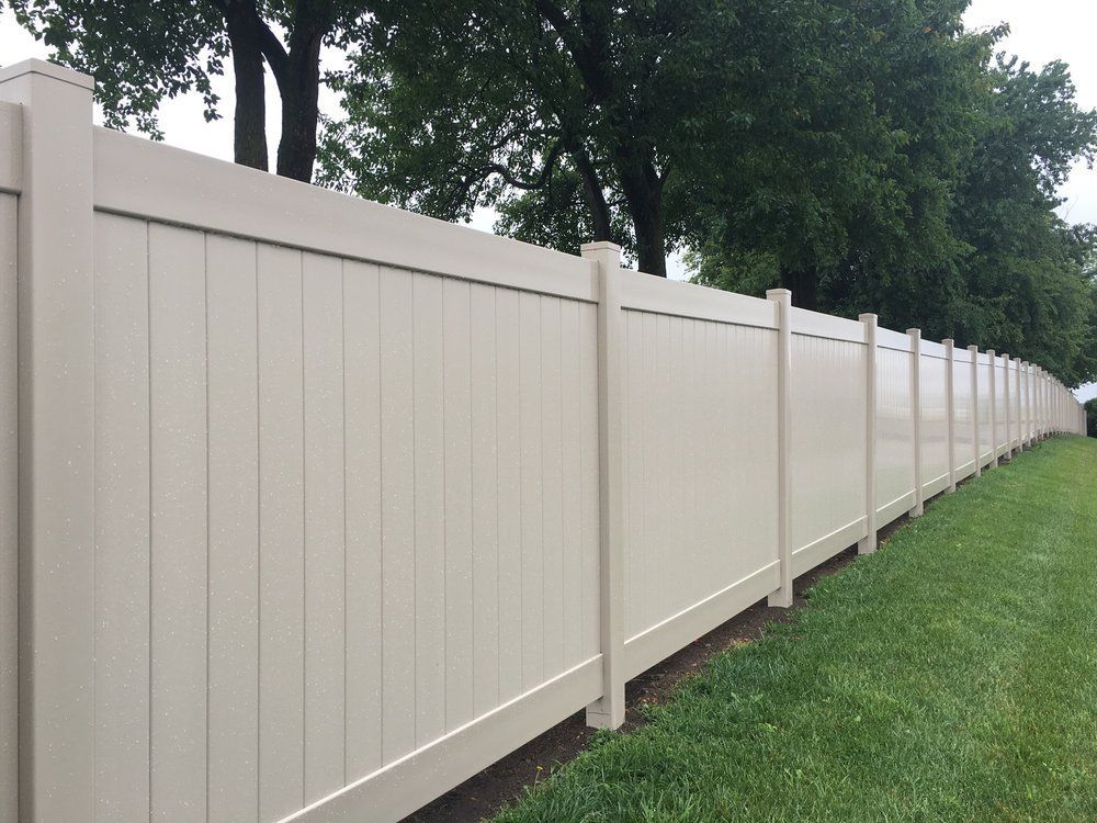 Beige vinyl fence along a green lawn with trees in the background.