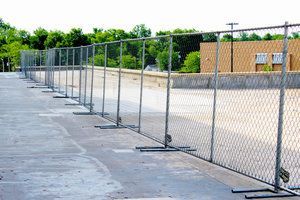 Chain-link fence sectioned off on a gray concrete surface, in front of a building, with green trees in the background.