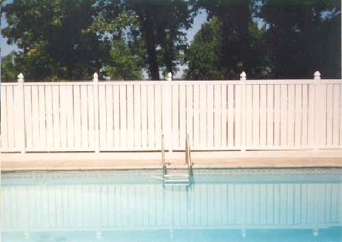 White fence surrounds a pool, ladder in the center. Trees are in the background.