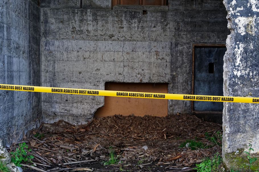 Yellow caution tape blocks a damaged concrete wall with debris on the ground.