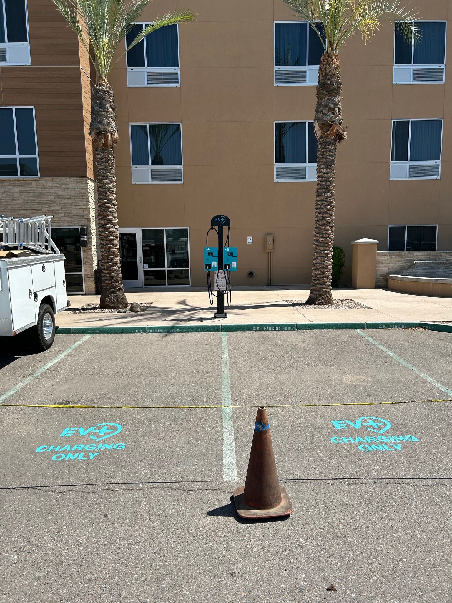Two parking spots marked with blue paint and a traffic cone in front of an electric vehicle charging station.