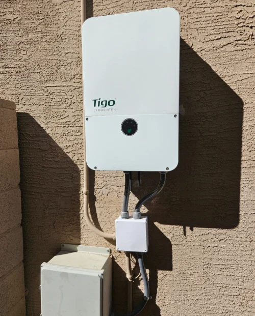A Tigo Energy power inverter mounted on an exterior stucco wall with conduit and a small junction box below.