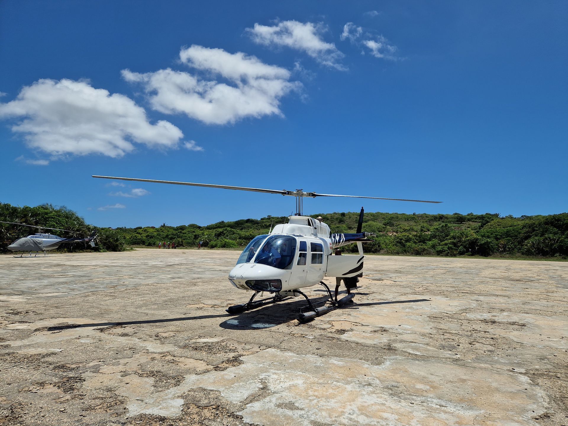 White helicopter on a rocky landing pad under a bright blue sky with scattered clouds.