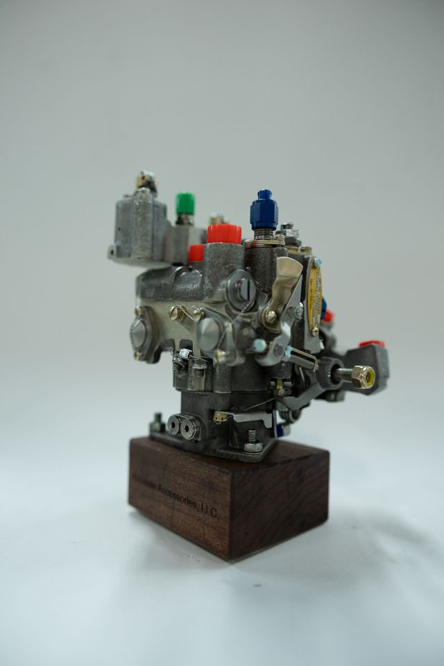Silver metal engine component with colorful caps on a wooden base.