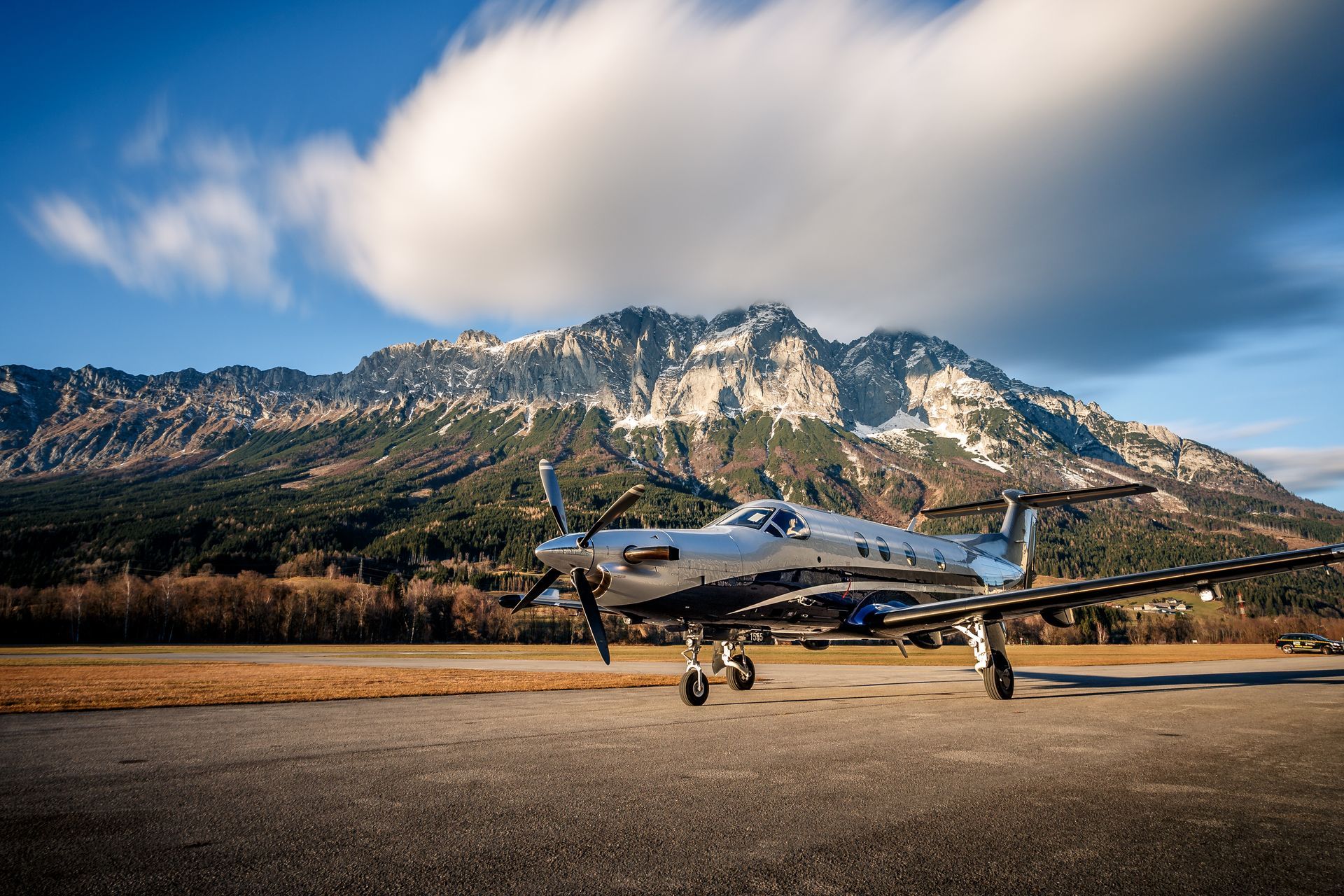 Airplane parked on a runway with a mountain range and cloudy sky in the background.