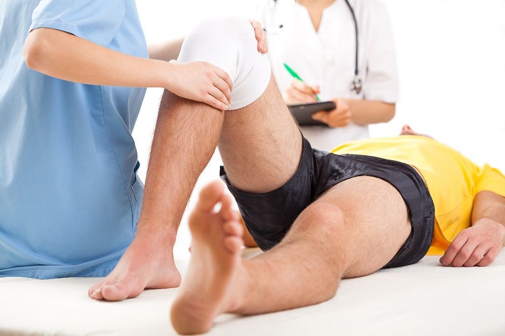 Person receiving medical attention for a knee injury. Two medical professionals assist.