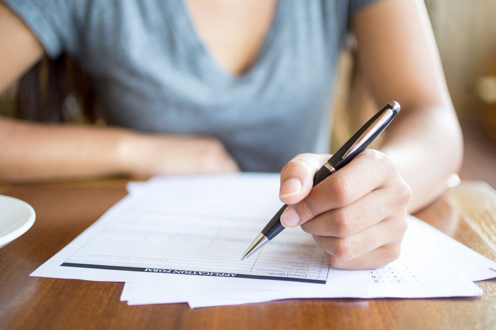 Woman with a pen writing on papers, sitting at a wooden table.