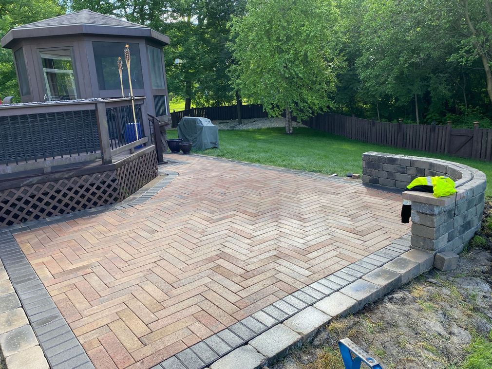 Backyard patio with herringbone pavers beside a gazebo, lawn, and stone planter wall