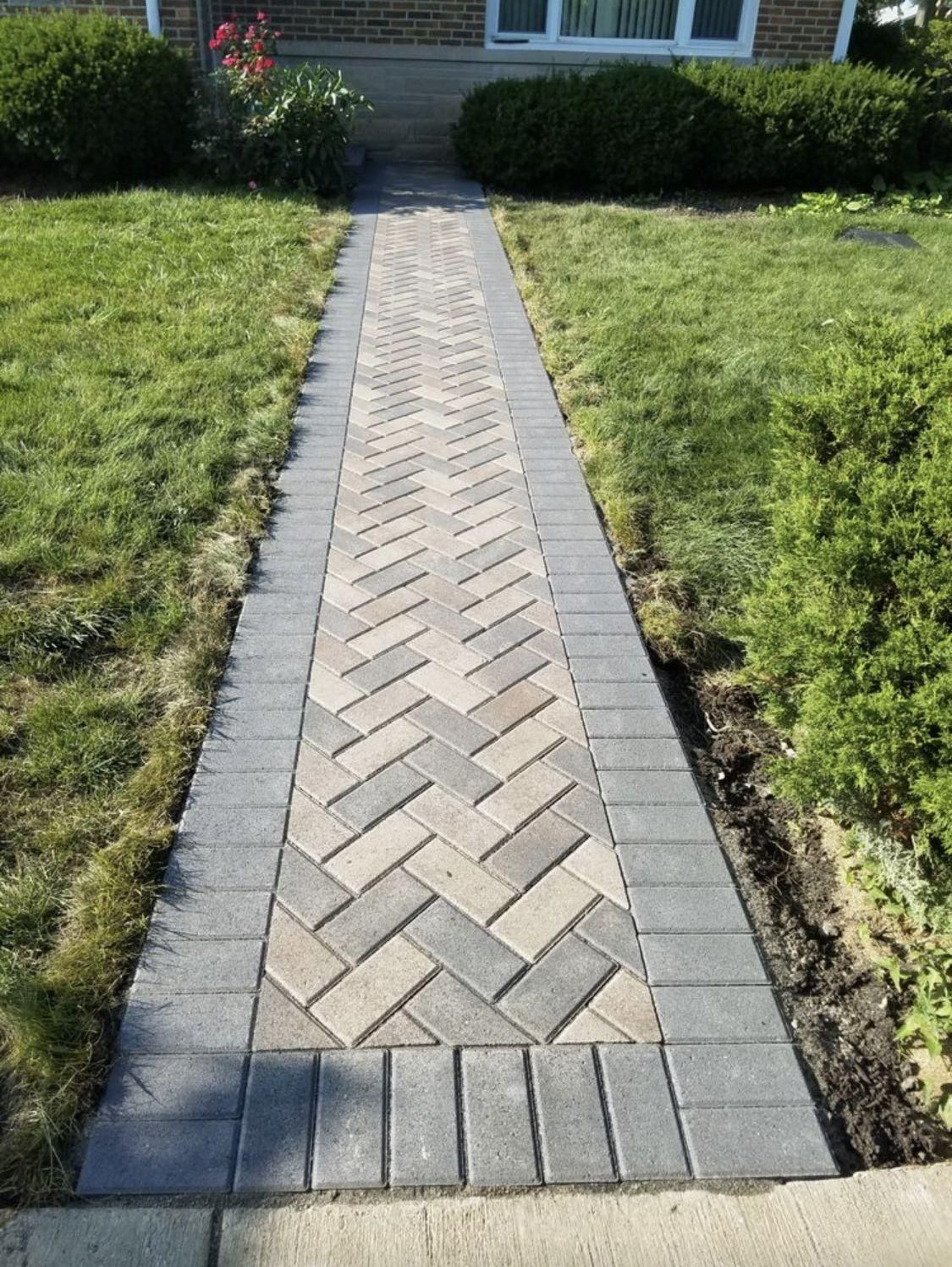 Brick walkway through a grassy front yard leading to a house entrance