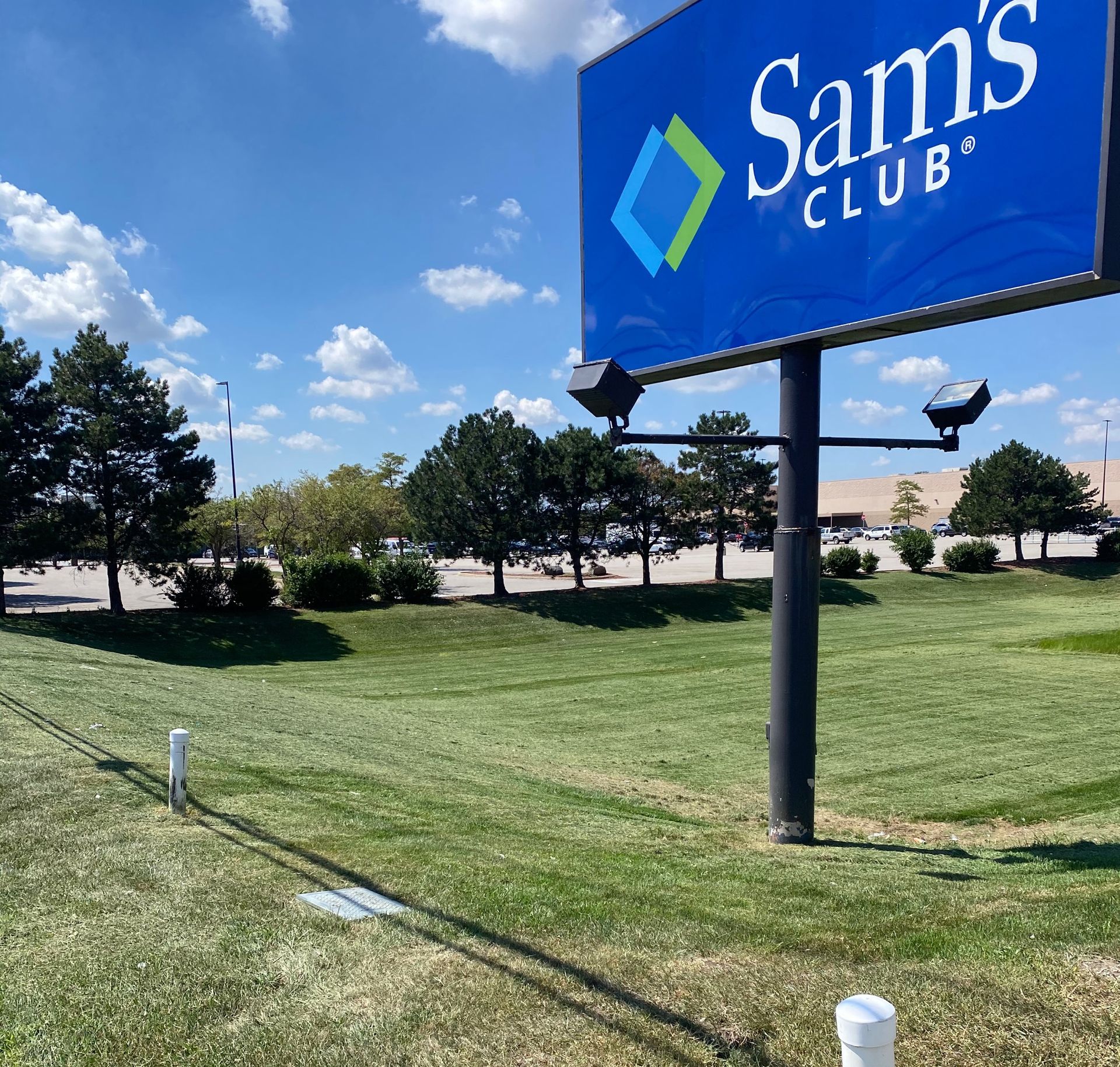 Sam’s Club sign on a sunny grassy roadside with blue sky and trees