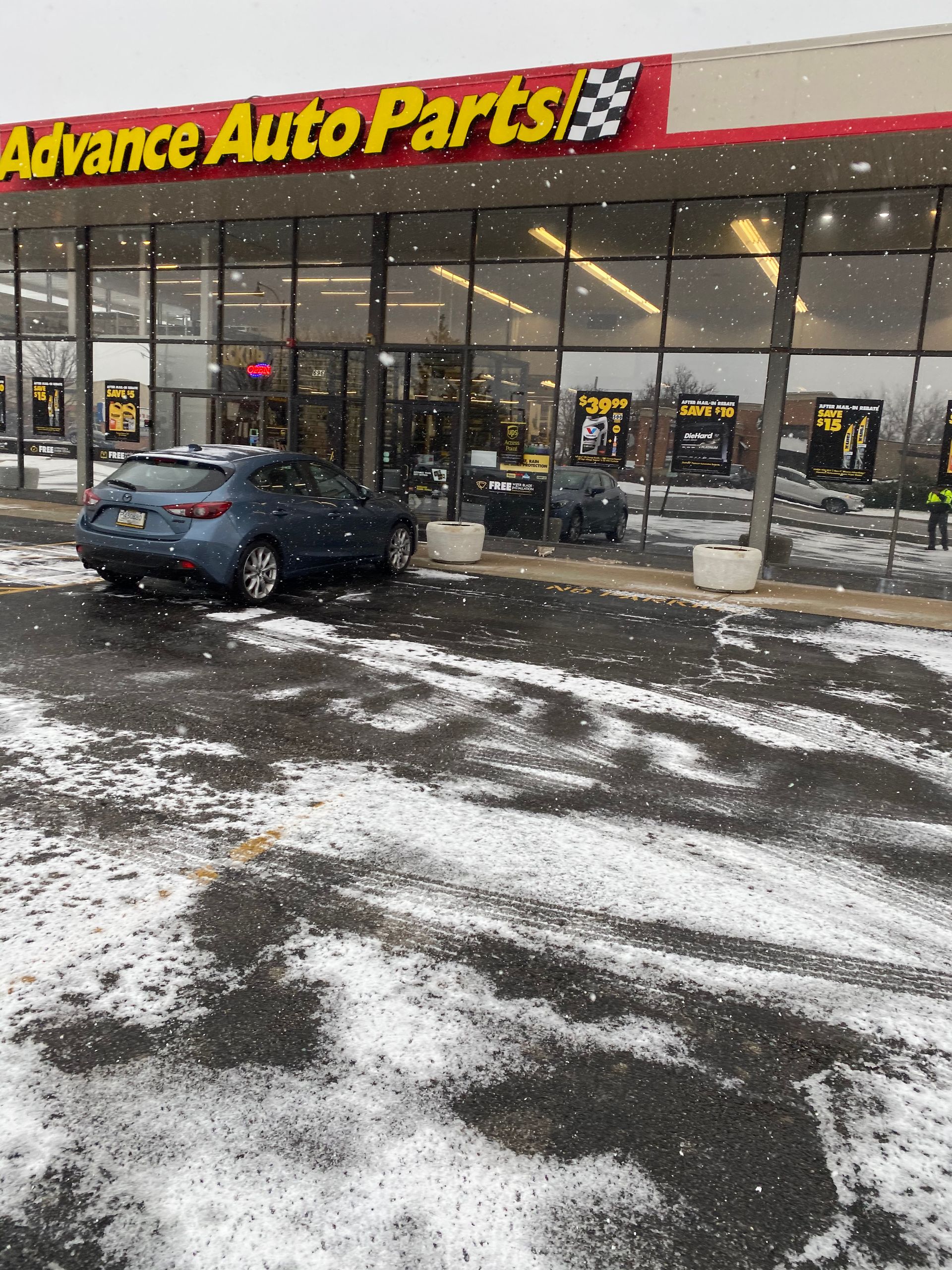 Snow-covered school building with a yellow plow clearing the blacktop driveway