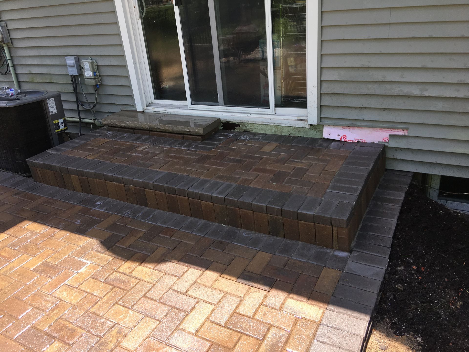 Brick back patio with steps leading to sliding glass doors beside a house.