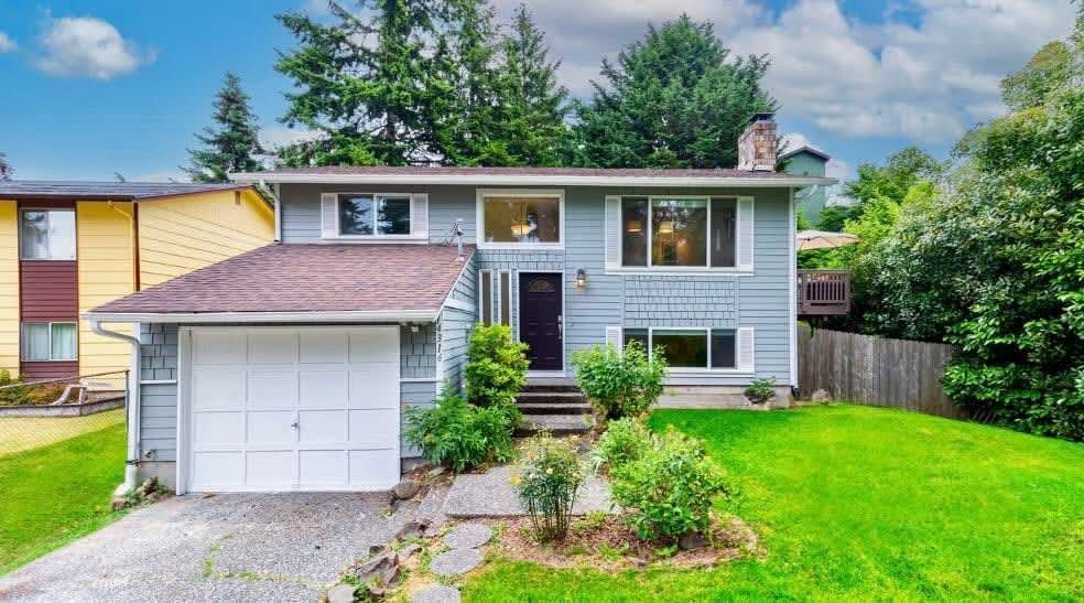 Suburban split-level house with white garage, gray siding, and green lawn under a blue sky