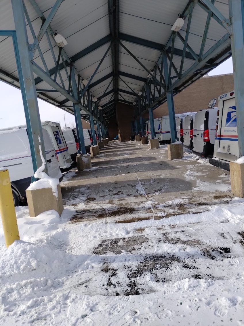 Snowy covered walkway between parked trucks under a metal canopy