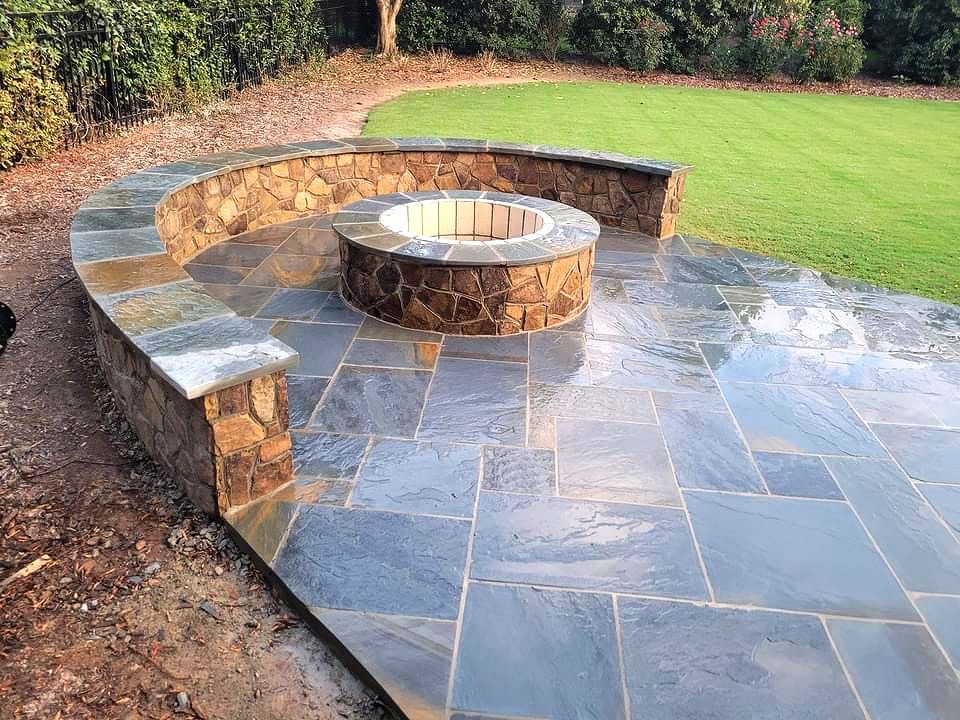 Curved stone bench and circular fire pit on a wet patio beside a green lawn