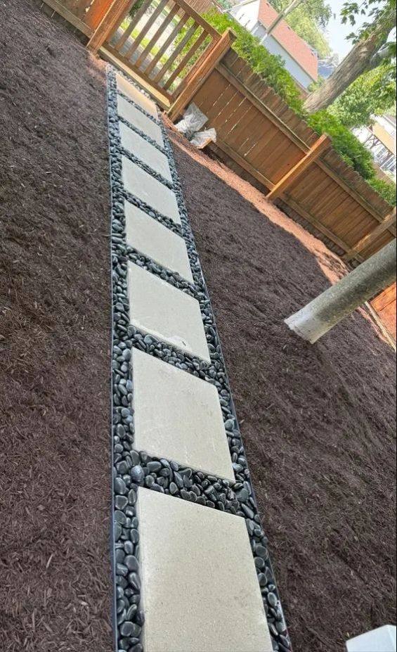 Stepping stone path through dark mulch in a fenced backyard garden
