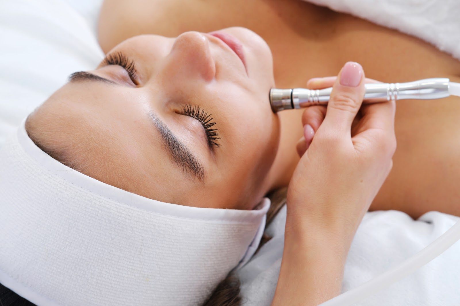 Woman receiving a facial treatment with a handheld skincare device and white headband