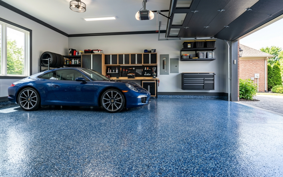A blue sports car parked inside a spacious garage with a glossy, blue-speckled epoxy floor and organized wall storage.