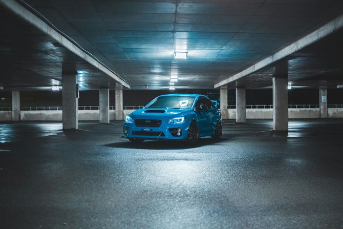 A bright blue Subaru WRX parked in the center of a dimly lit concrete parking garage at night.