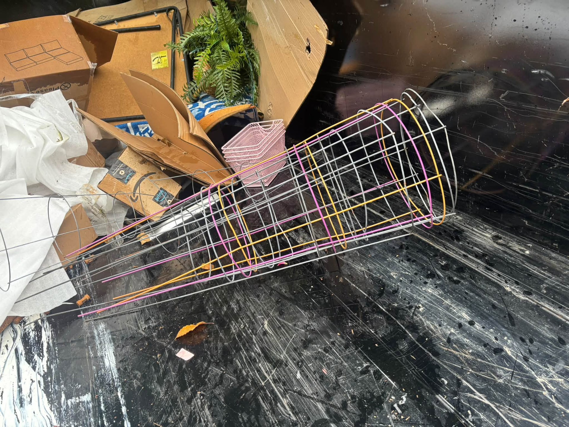 Collapsed wire pet cage in a trash pile on a dumpster floor, surrounded by cardboard and debris