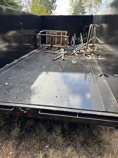 Empty black trailer bed with scattered metal frames and debris, viewed from the rear outdoors.