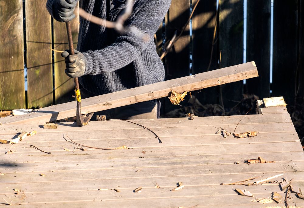 Person using a hammer and pry bar to lift boards on a wooden roof or deck under construction