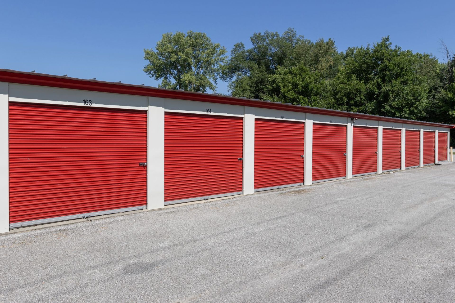 Red storage unit doors with white frames along a gravel lot under a blue sky