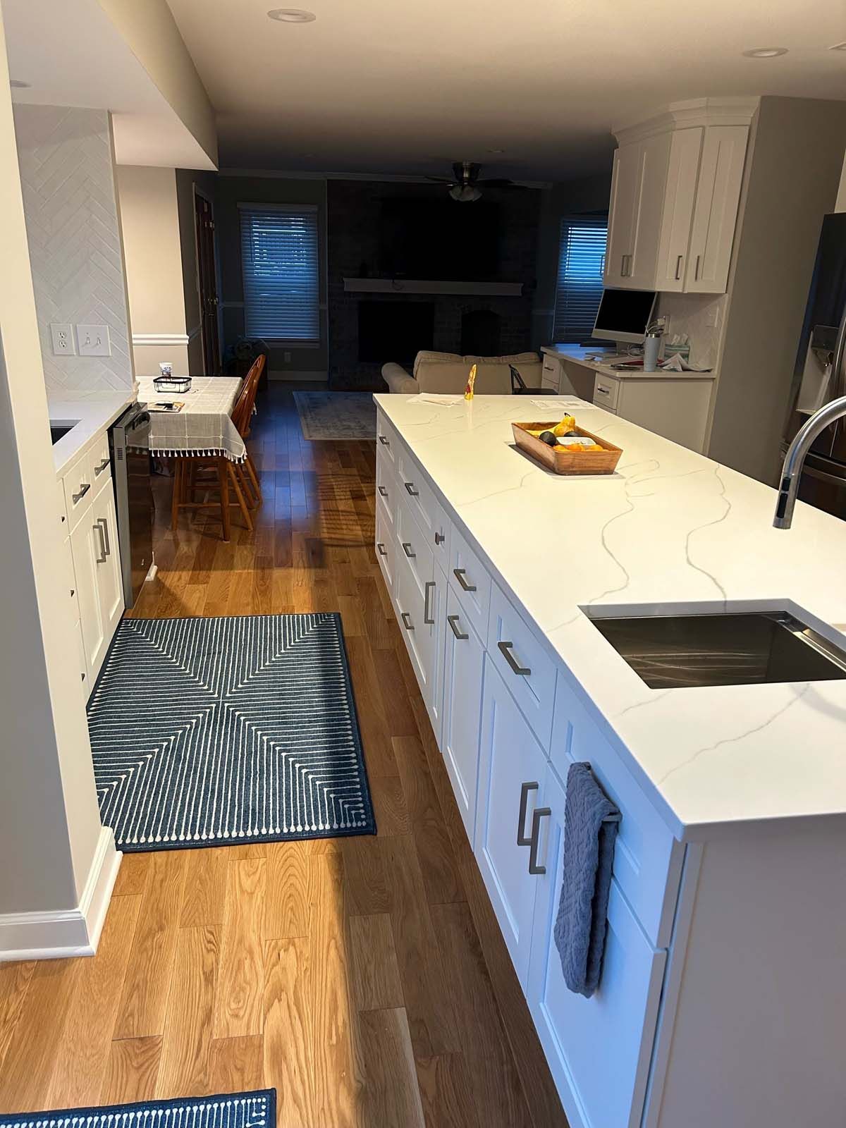 Modern kitchen with white cabinets, long island, wood floor, and view into living room.