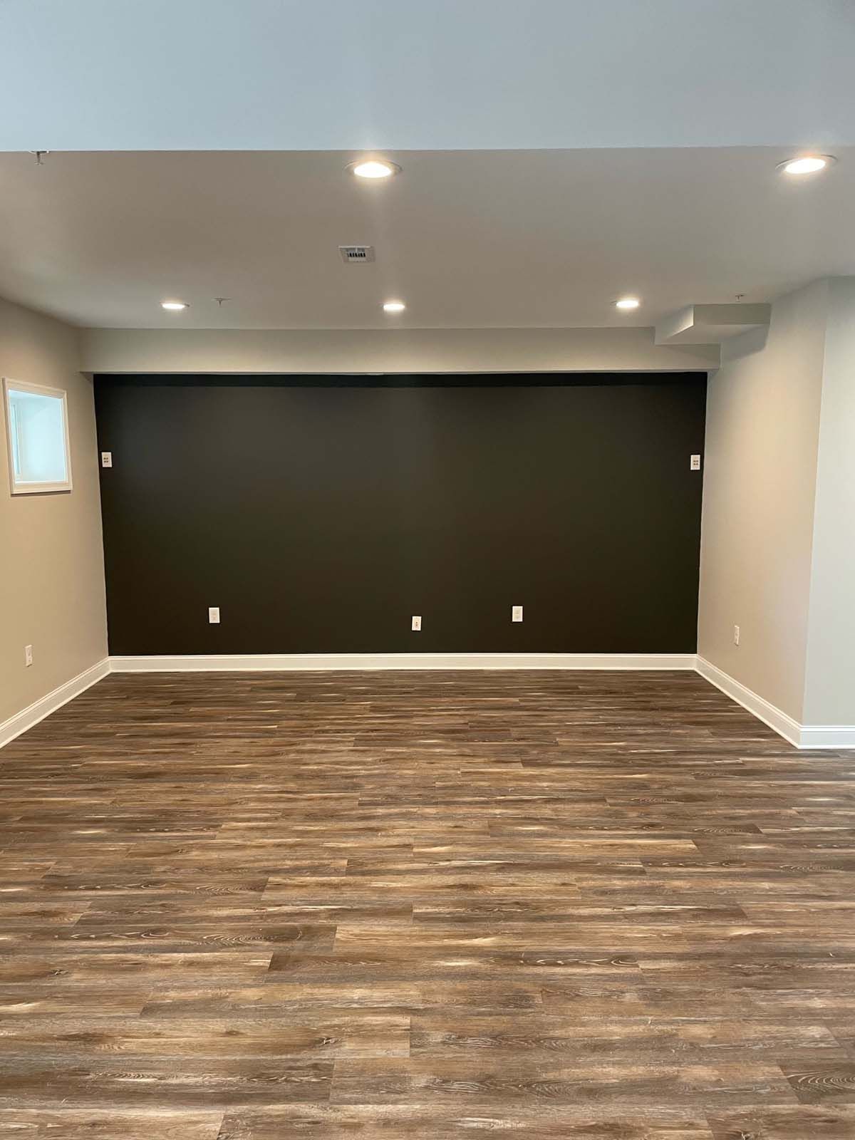 Dark-painted wall in a room with wood flooring and recessed lighting; electrical outlets are visible on the wall.