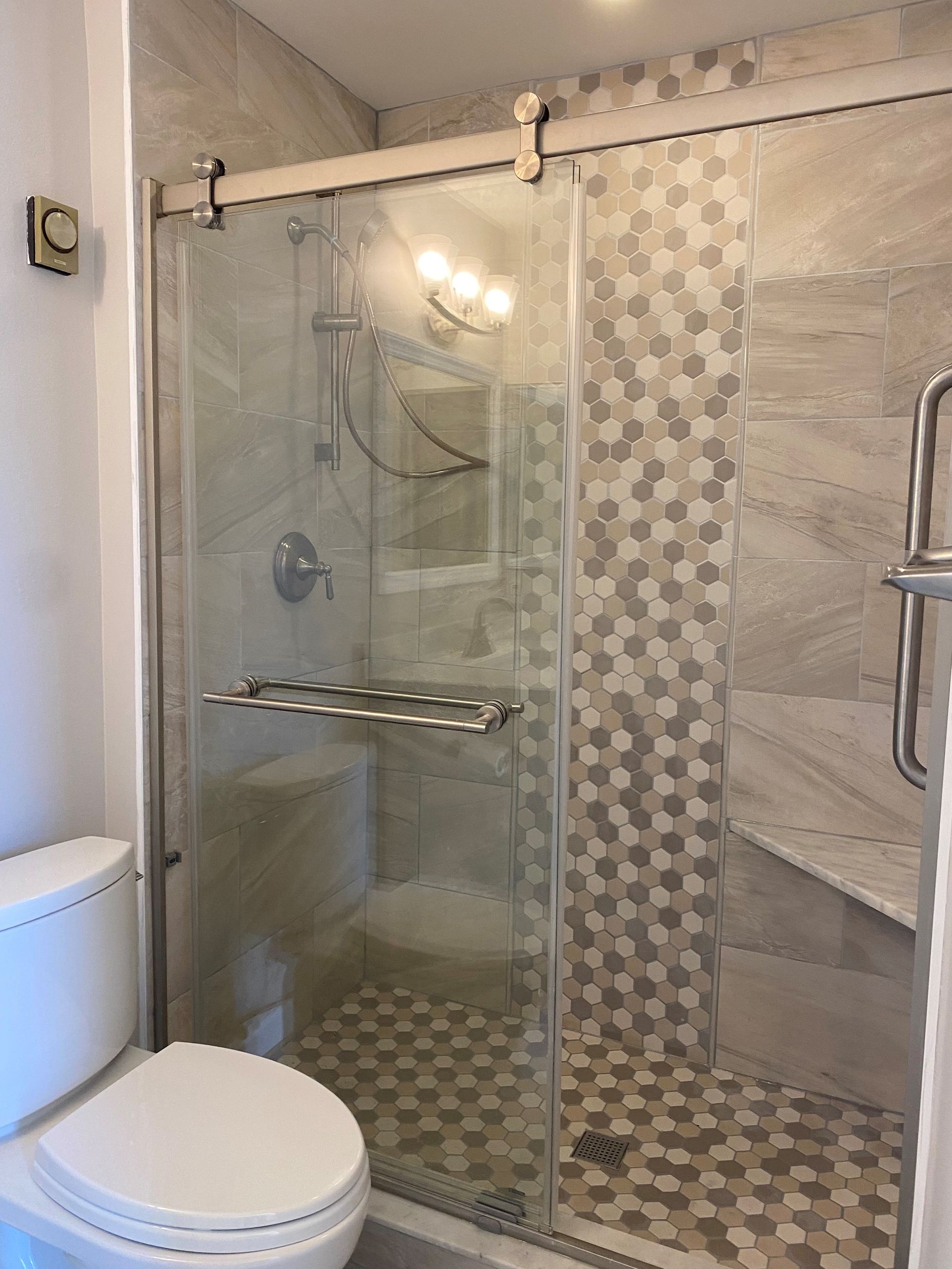Bathroom with glass shower, white toilet, and patterned tile.