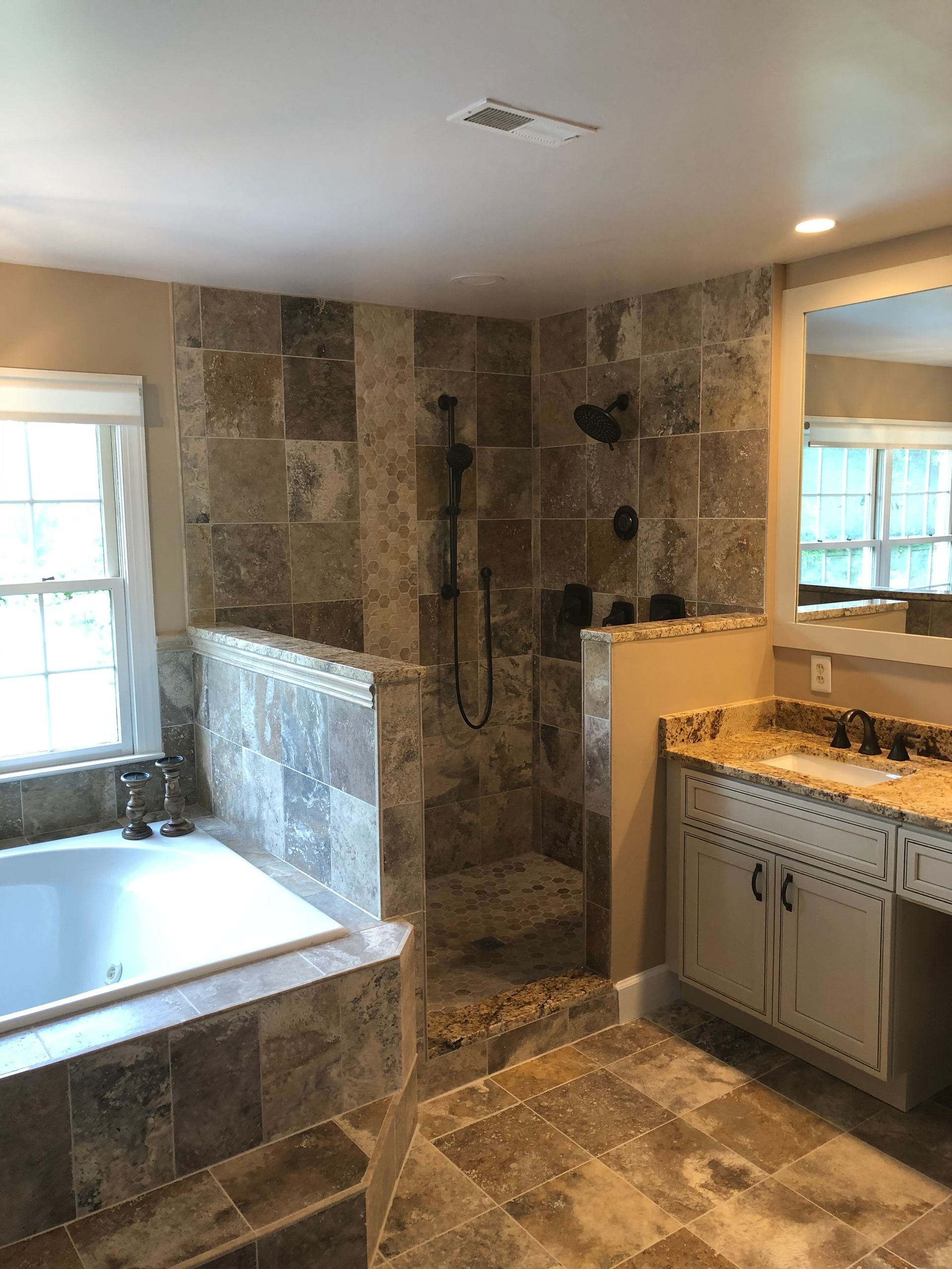 Bathroom with a shower, tub, and vanity; stone tile walls and floors.