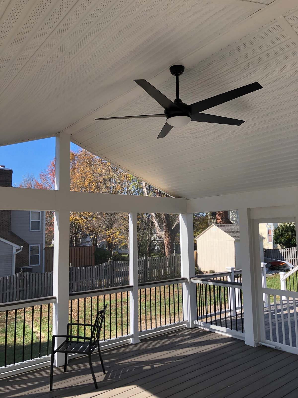 Covered outdoor deck with black ceiling fan, black metal railings, and a chair.