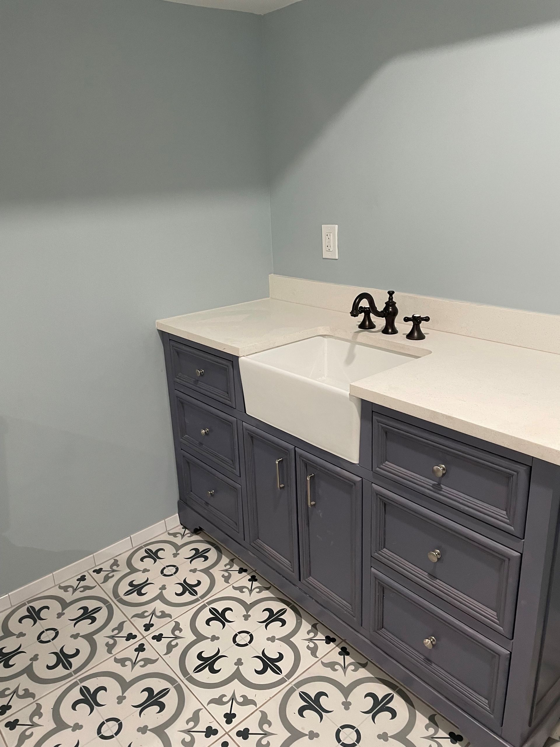 Bathroom vanity with blue cabinets, white countertop, and patterned floor tiles.