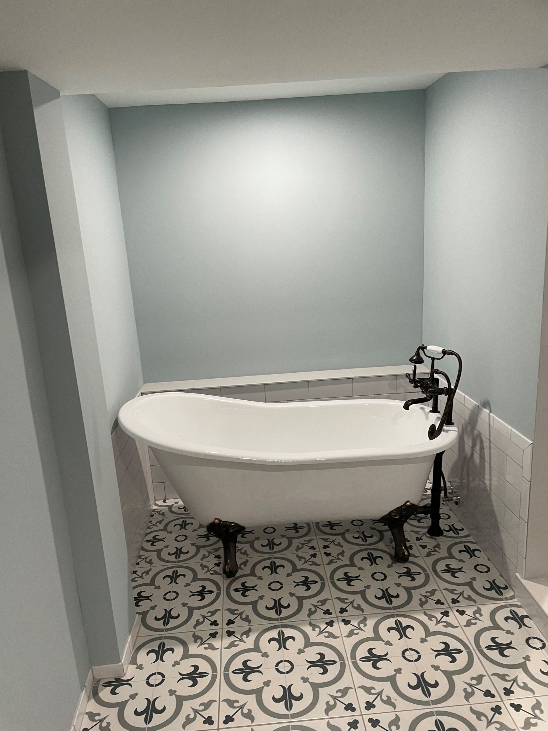 Claw-foot bathtub in a small, pale blue-walled bathroom with patterned floor tiles.
