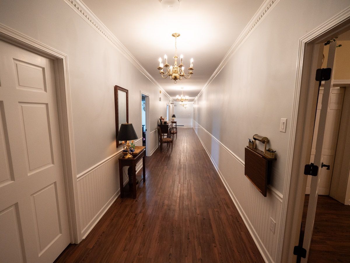 Long hallway with red carpet, cream walls, framed artwork, and chandelier.