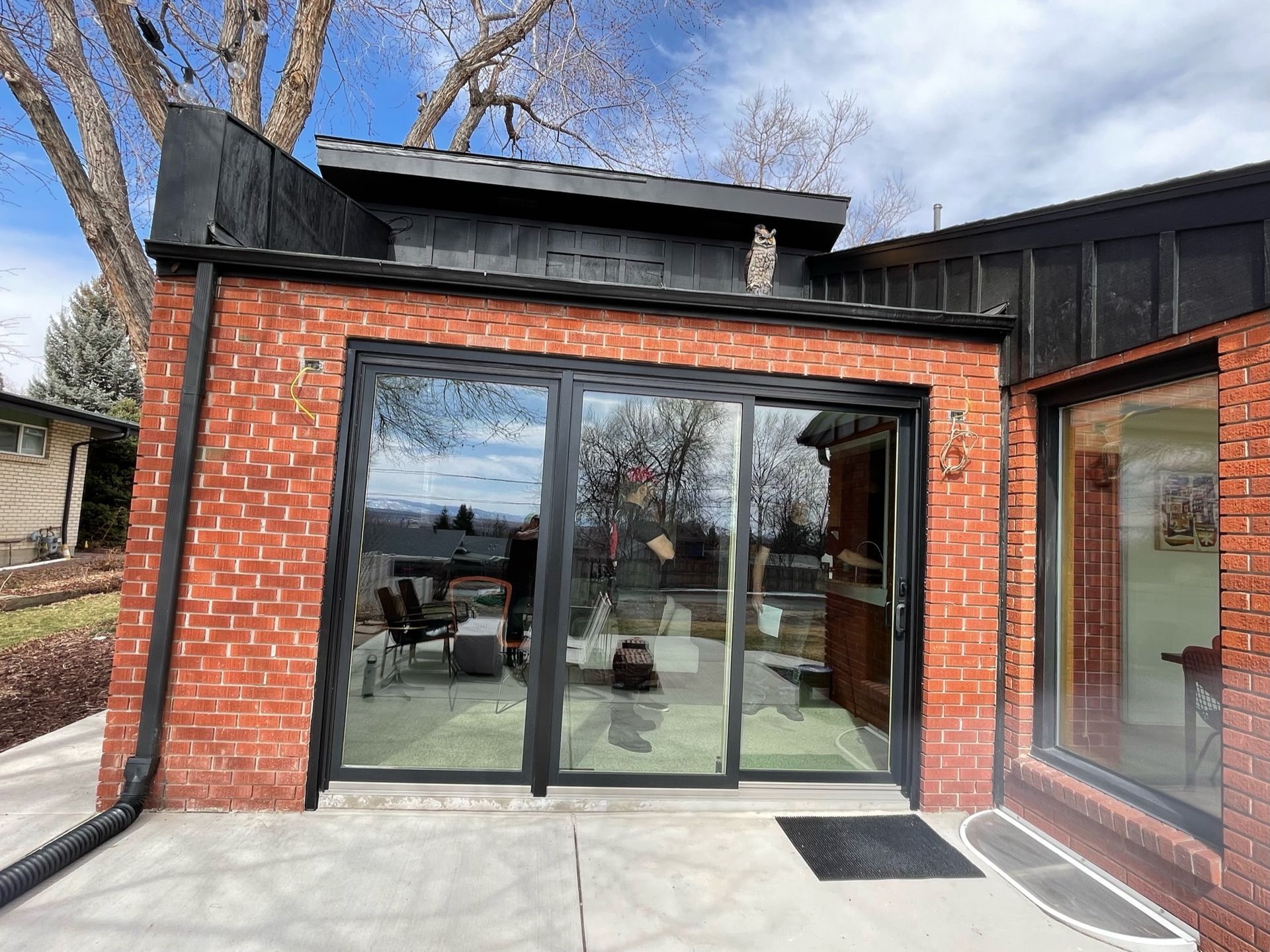Brick-walled modern home extension with glass sliding doors, black trim, and a patio, reflecting a view inside.