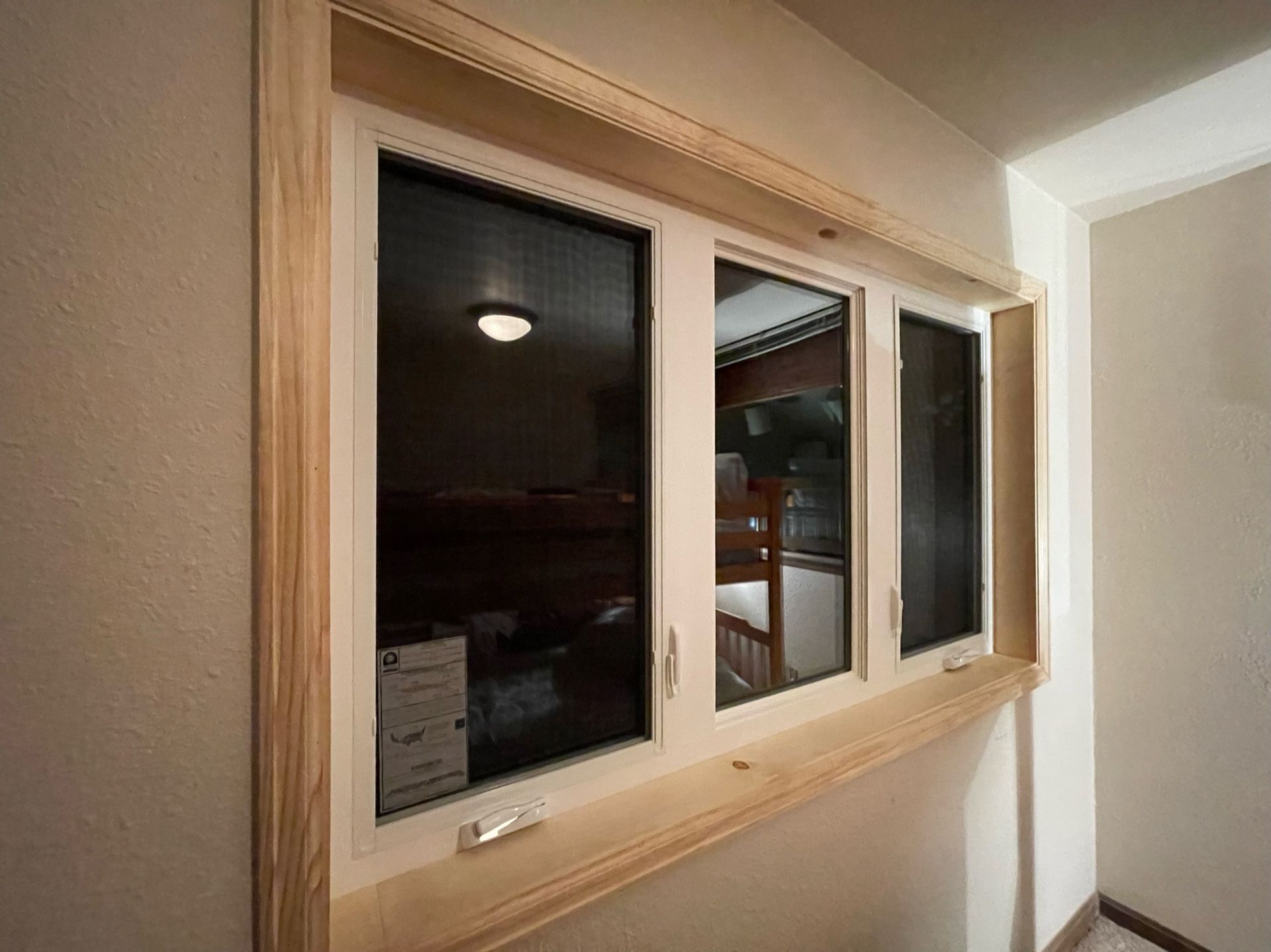 Wooden-framed, triple-pane window with white trim, set in a light-colored wall. Interior view with dark reflections.