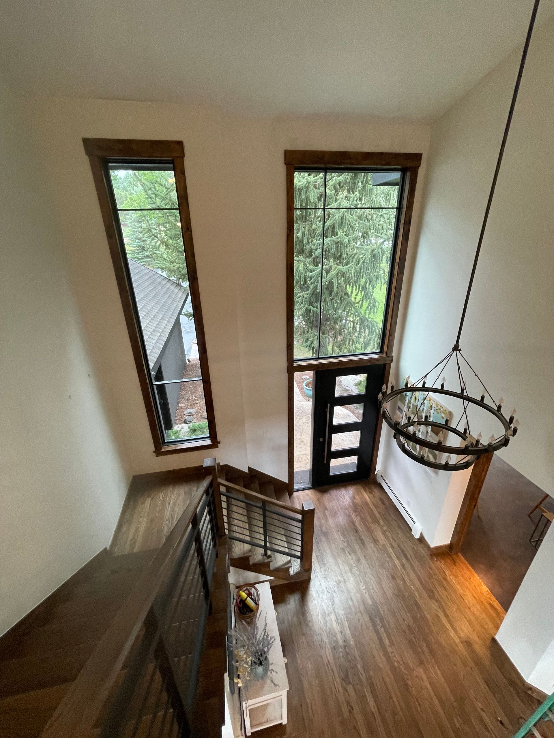 Stairwell with hardwood floors and dark wooden trim windows, black door, and chandelier.