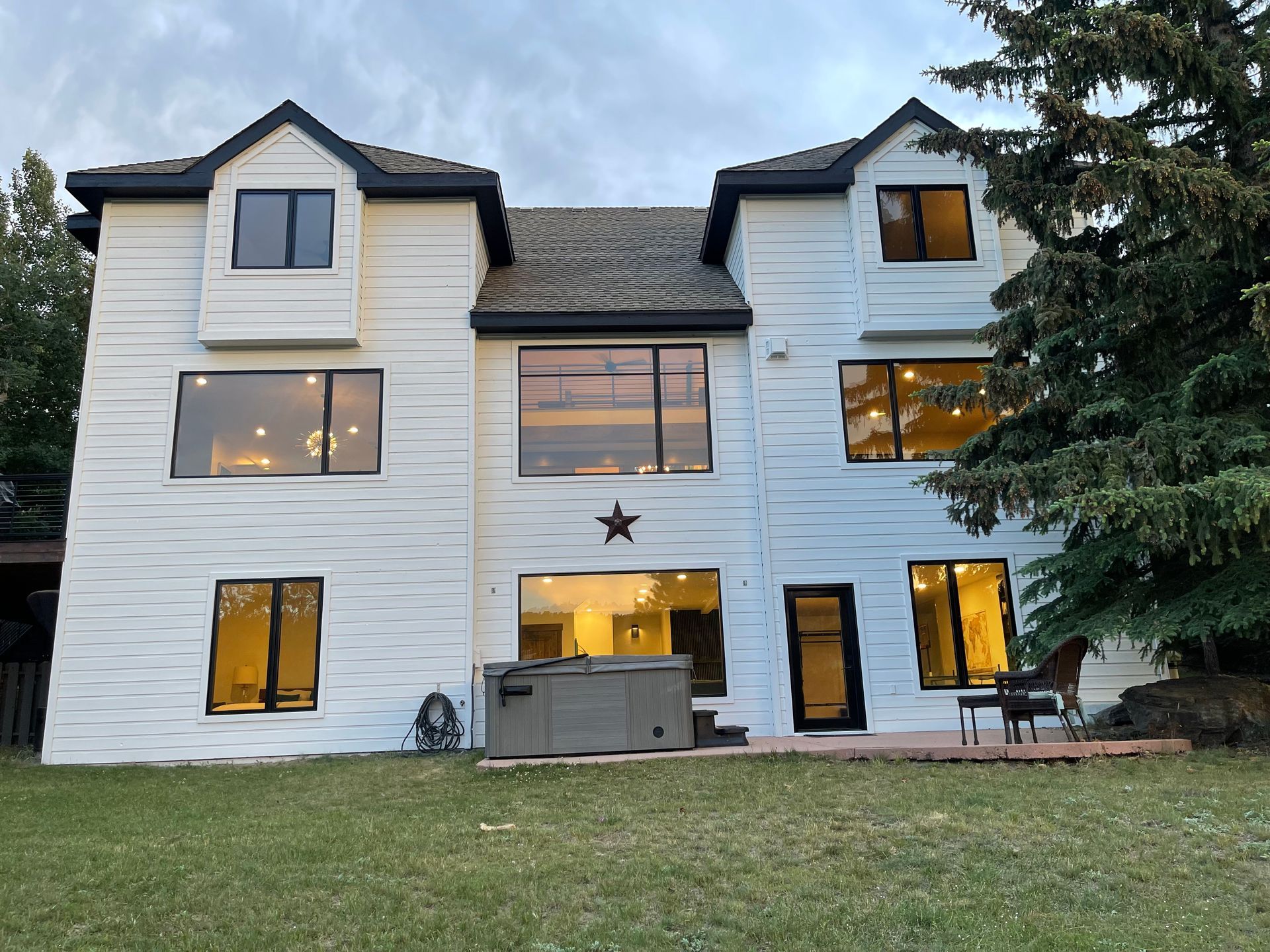 White two-story house with dark trim and large windows, a hot tub, and a grassy lawn.